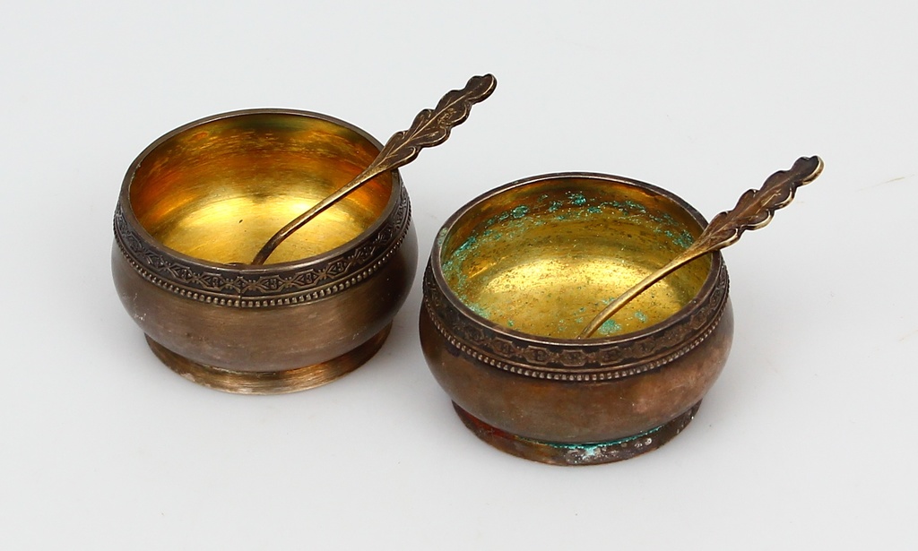 Two metal spice dishes with two silver spoons