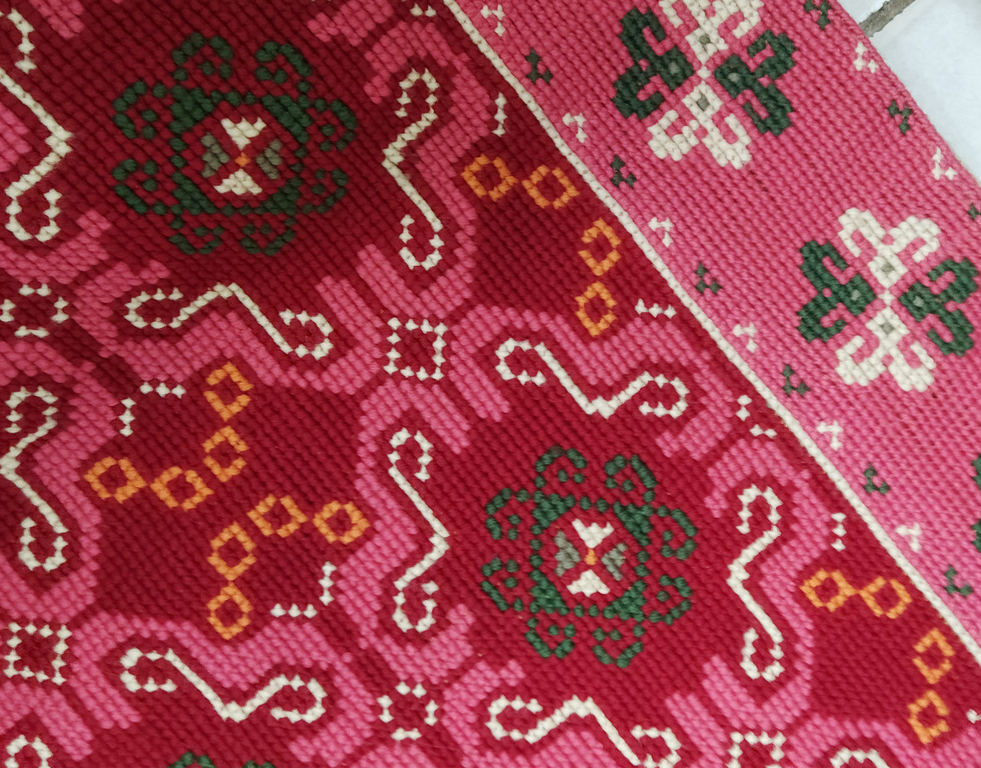 Woven wall covering with Latvian patterns in pink tones